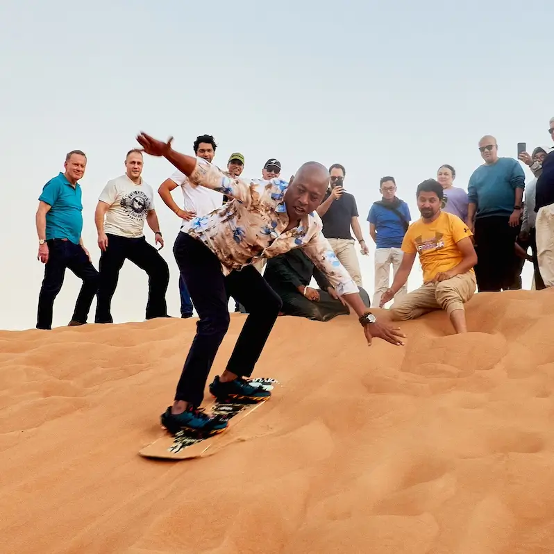 Persone che scendono su una tavola sulle dune del deserto